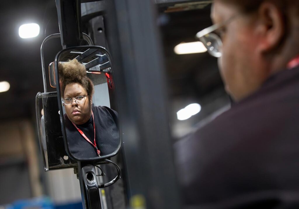 `VersAbility Tech forklift trainee checking the side mirror for safety before moving.``