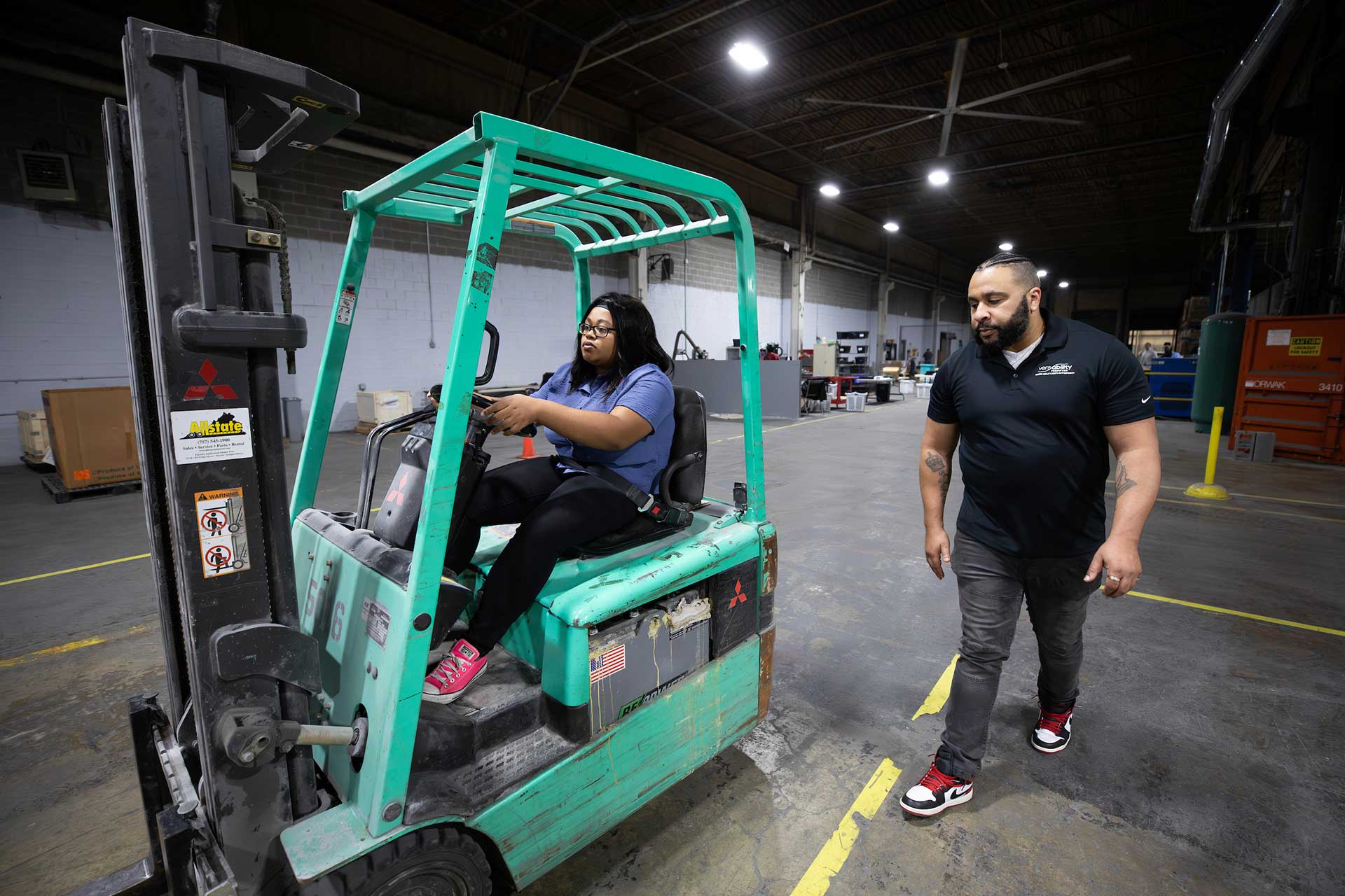 VersAbility TECH instructor walking alongside a student operating a forklift in a warehouse.