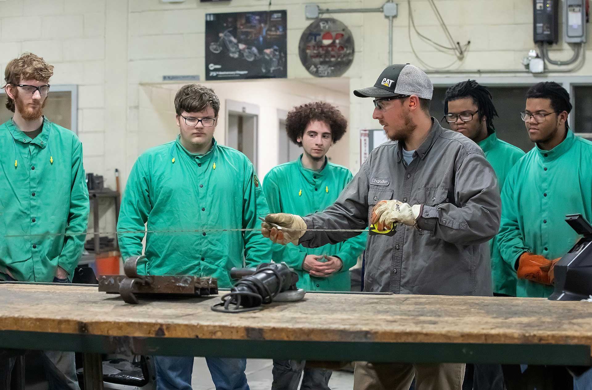 Instructor demonstrating a welding technique to a group of VersAbility TECH students in green jackets.