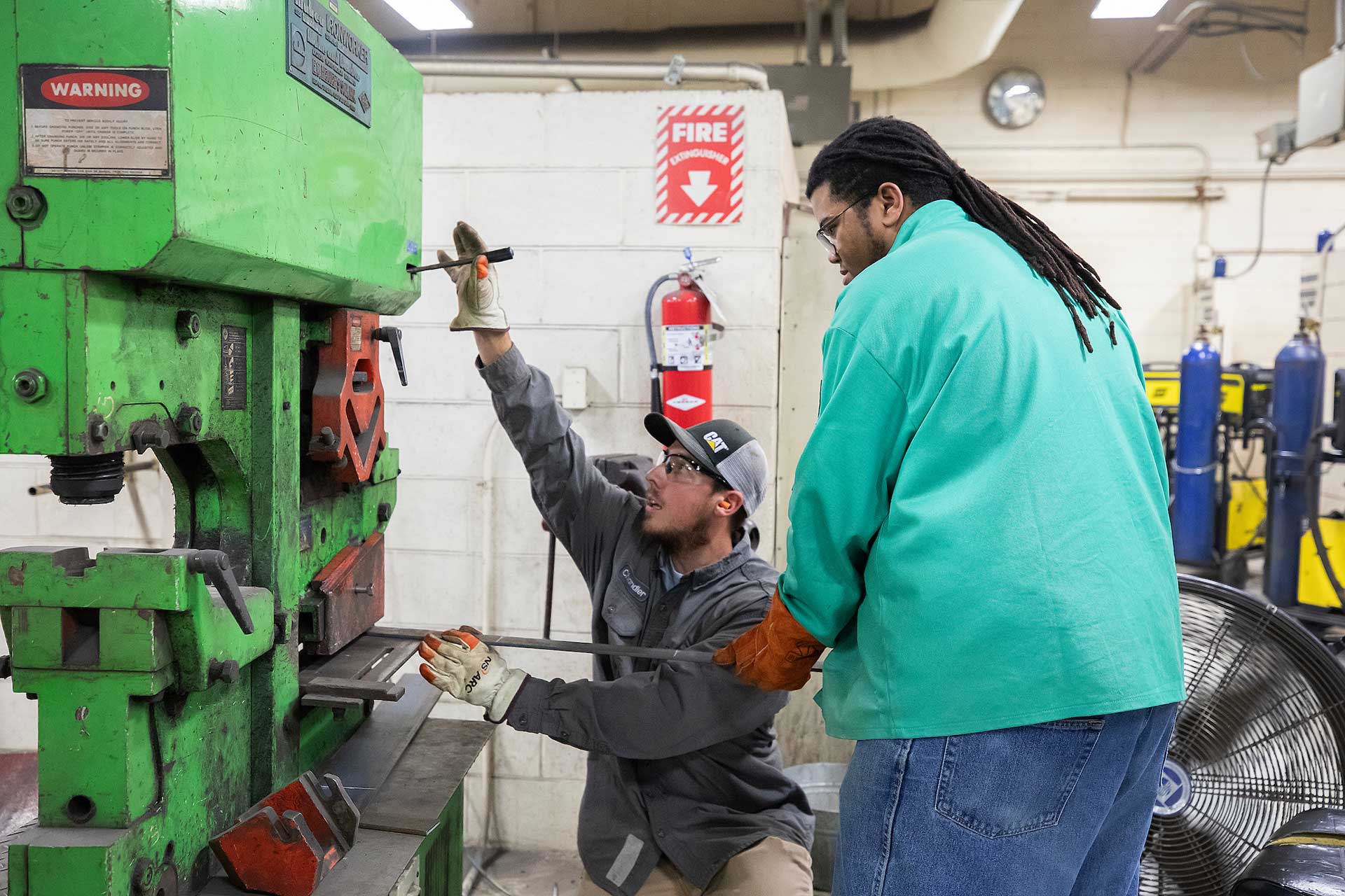 Instructor coaching a VersAbility TECH student on how to use a large green metal fabrication machine.