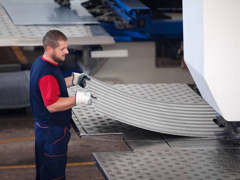 A man fabricates a metal sheet in a factory, focused on his work with tools and machinery around him.