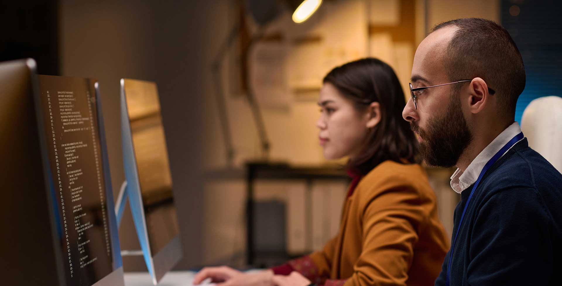 Side view portrait of two software developers using computers and writing code sitting at workplace in office